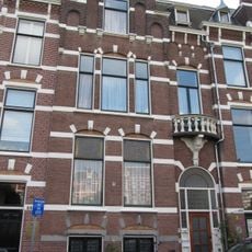 Pand in neo-renaissance trant met trapgevel, waarin ontlastingsbogen, blokken en banden. Rechts een terugliggende ingangspartij met boogfries en balcon met balustrade
