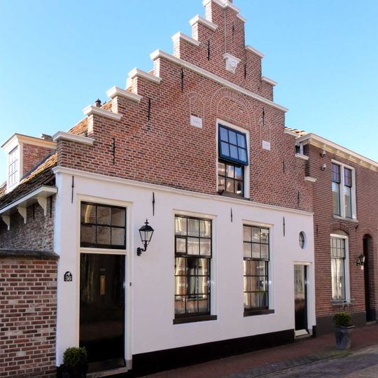 Pand met beneden gepleisterde trapgevel met zandstenen waterlijsten en afdekplatenen uitgekraagde toppilaster op zandstenen console met leeuwenmasker