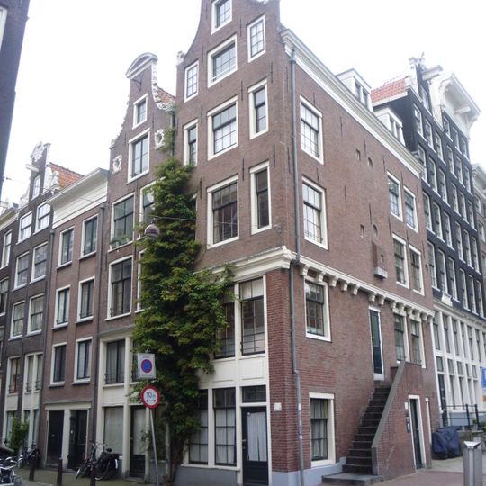 Hoekhuis waarvan de voorgevel een latere rollagentop heeft en de zijgevel op balkknoppen is overgebouwd