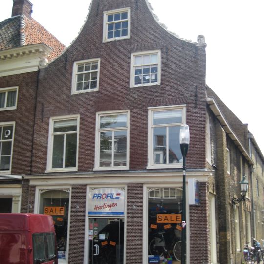 Diep pand onder zadeldak tegen hoge klokgevel met natuurstenen aanzetkrullen en achterhuis van gele steen