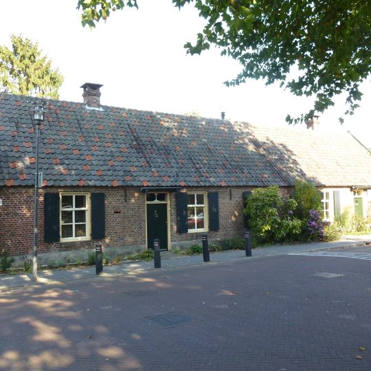 Landarbeiderswoning bestaand uit twee evenwijdige vleugels onder zadeldaken met riet en pannen gedekt. Vensters met zesruitsschuiframen