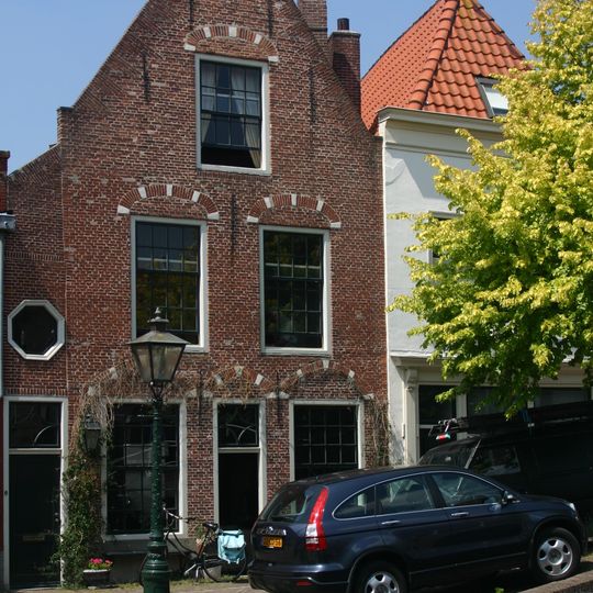 Pand met bakstenen gevel met vlechtingen, boven de ramen van de eerste verdieping korfbogen. Ondergevel gepleisterd