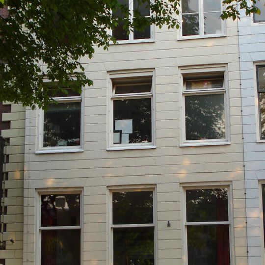 Gepleisterd koopmanshuis met eenvoudige lijstgevel. Onder de kroonlijst liggende vensters, gescheiden door triglyfen