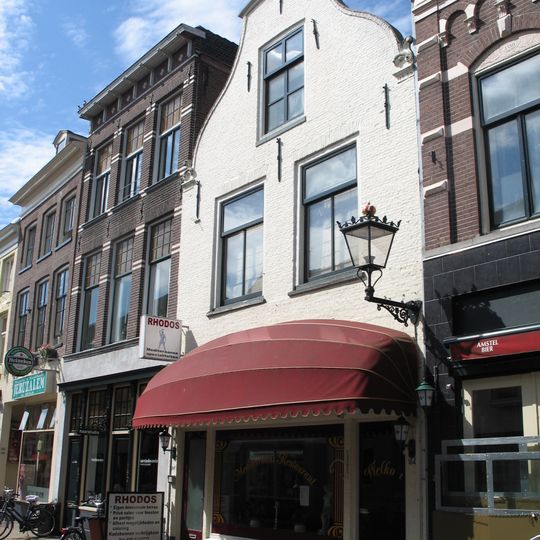 Huis met geverfde in- en uitgezwenkte topgevel, siersteen en jongere winkelpui