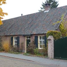 Landarbeiderswoning, bestaand uit twee evenwijdige vleugels onder zadeldaken met riet en pannen gedekt. Vensters met zesruitsschuiframen.