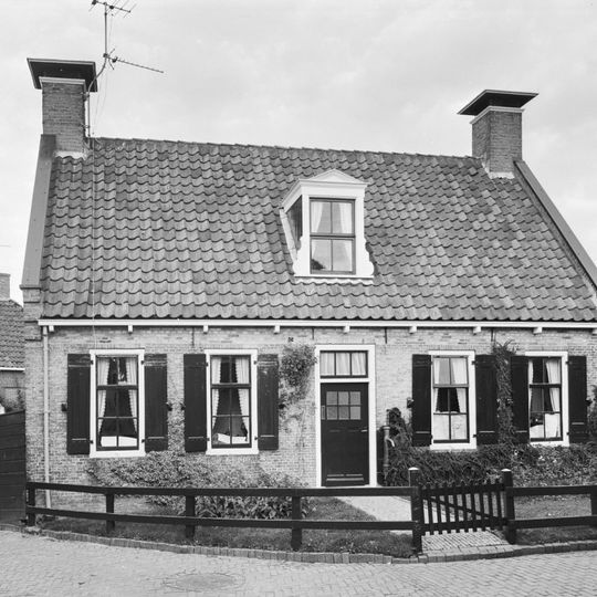 Laag pand onder zadeldak tussen topgevels met schoorstenen waarop borden en met dakkapel met klauwstukken en driehoekig fronton