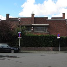 Twee geschakelde herenhuizen die onder een hoek van 45 graden ten opzichte van de rechthoekige kruising liggen, bestaande uit twee bouwlagen onder platte daken