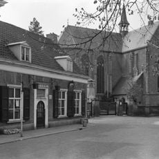 Laag dorpshuis in gele baksteen met zadeldak mede van belang door situatie naast kerk