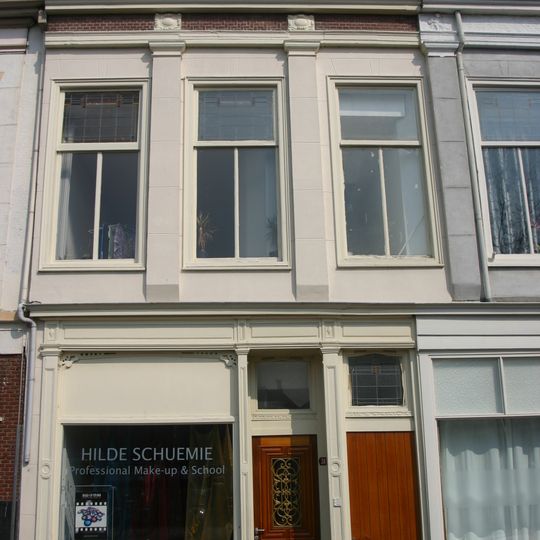 Pand met verminkte bakstenen gevel met rechte kroonlijst. De verdieping voorzien van Dorische pilasterstellingen en fries van metselmozaïek