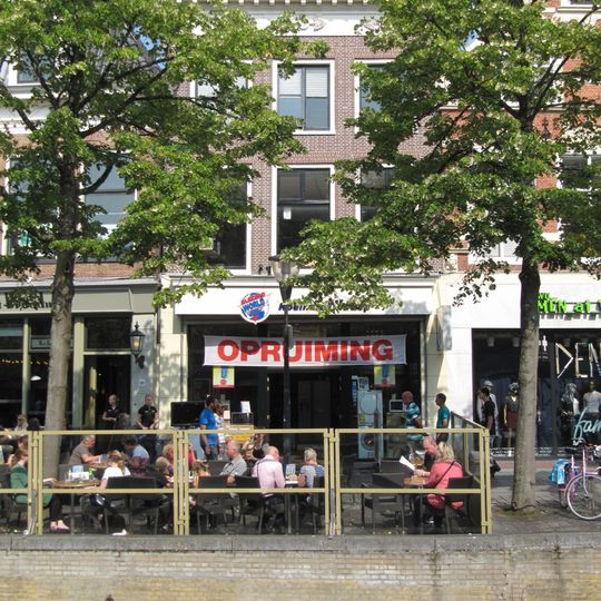 Eenvoudig pand onder voor afgeschuind zadeldak met geblokte kroonlijst waarop gietijzeren ornamenten