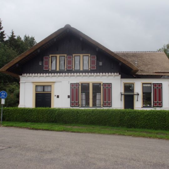 Gedeeltelijk bepleisterde chaletachtige dienstwoning. Rieten dak, venster met merkwaardige verdeling