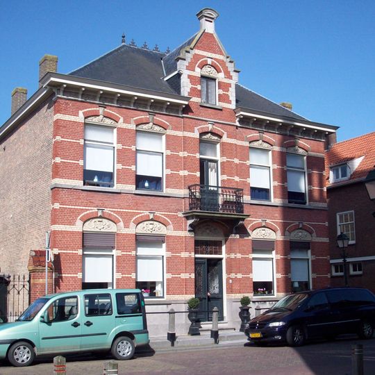 Herenhuis, gebouwd in eclectische stijl met natuurstenen stoep, stoeppalen en ten zuiden aan de voorgevel een ijzeren hekwerk tussen rode bakstenen kolommen