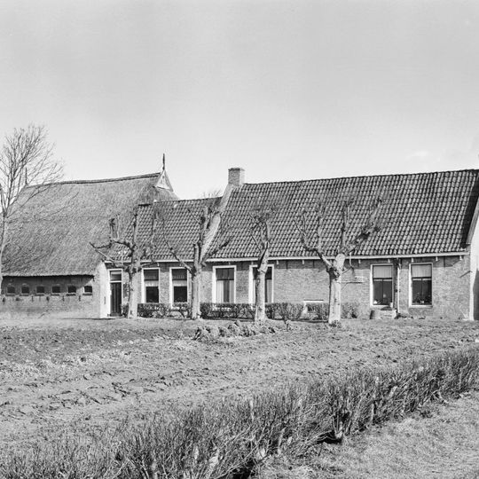 Kop-hals-rompboerderij met in het midden onderkelderd lang voorhuis onder zadeldak tussen topgevels waarvan de voorste vrijwel gesloten