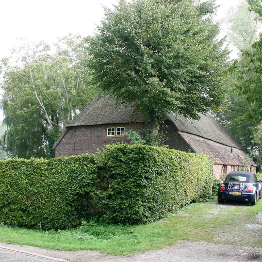 Boerderij onder met riet en pannen gedekt schilddak, dat aan de achterzijde is afgewolfd. Hoekhuis van het kortgeveltype met dwarsdeel