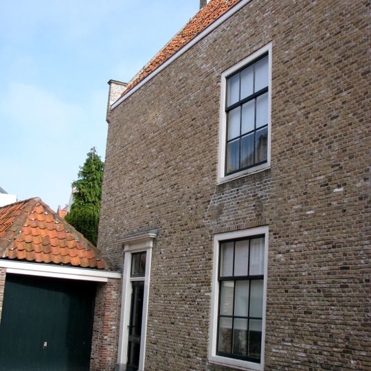 Huis met gedeeltelijk ontpleisterde trapgevel. De treden afgedekt met natuurstenen platen. Waterlijsten. Boven de vensters accoladebogen, die een paar ontlastingsboogjes omvatten