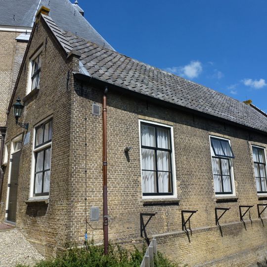 Tegen de z.o.zijde van het koor een huisje met zadeldak en puntgevel met rollaag, gedateerd in een steen