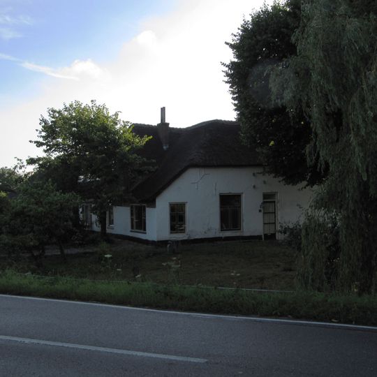 Deels gepleisterde hoeve met rechts een opkamer. Omlopend rieten schilddak. Langgerekte stal met pannen zadeldak en bewerkte daklijst