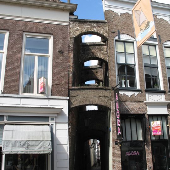 Pand met jongere winkelpui in versierde gevel en met gemetselde schoren die de Houtzagersteeg tussen de nrs. 162 en 164 overspannen