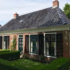 Dubbel landelijk pand met stichtingssteen en goot op klossen onder schilddak met twee hoekschoorstenen (vormt een geheel met nr. 27)