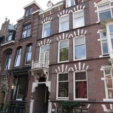 Pand in neo-renaissance trant. Souterrain. Gevelversiering met geblokte vensterstrekken en gekoppelde ontlastingsboogjes. Boven de ingang een houten balcon