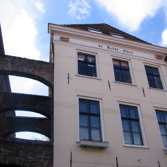 Rijzig pand met forse lijst, gewijzigde pui en vensters en met gemetselde boogvormige schoren die de Koldenhovensteeg tussen de nrs. 96 en 98 overspannen