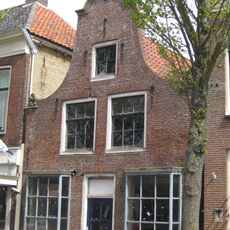 Pand met gerestaureerde vensters en pui onder zadeldak tegen klokgevel met aanzetkrullen en kuifstuk